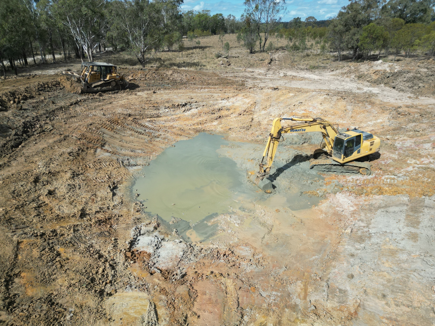 Aerial view of an excavator and CAT dozer desilting a farm dam with muddy water in the base