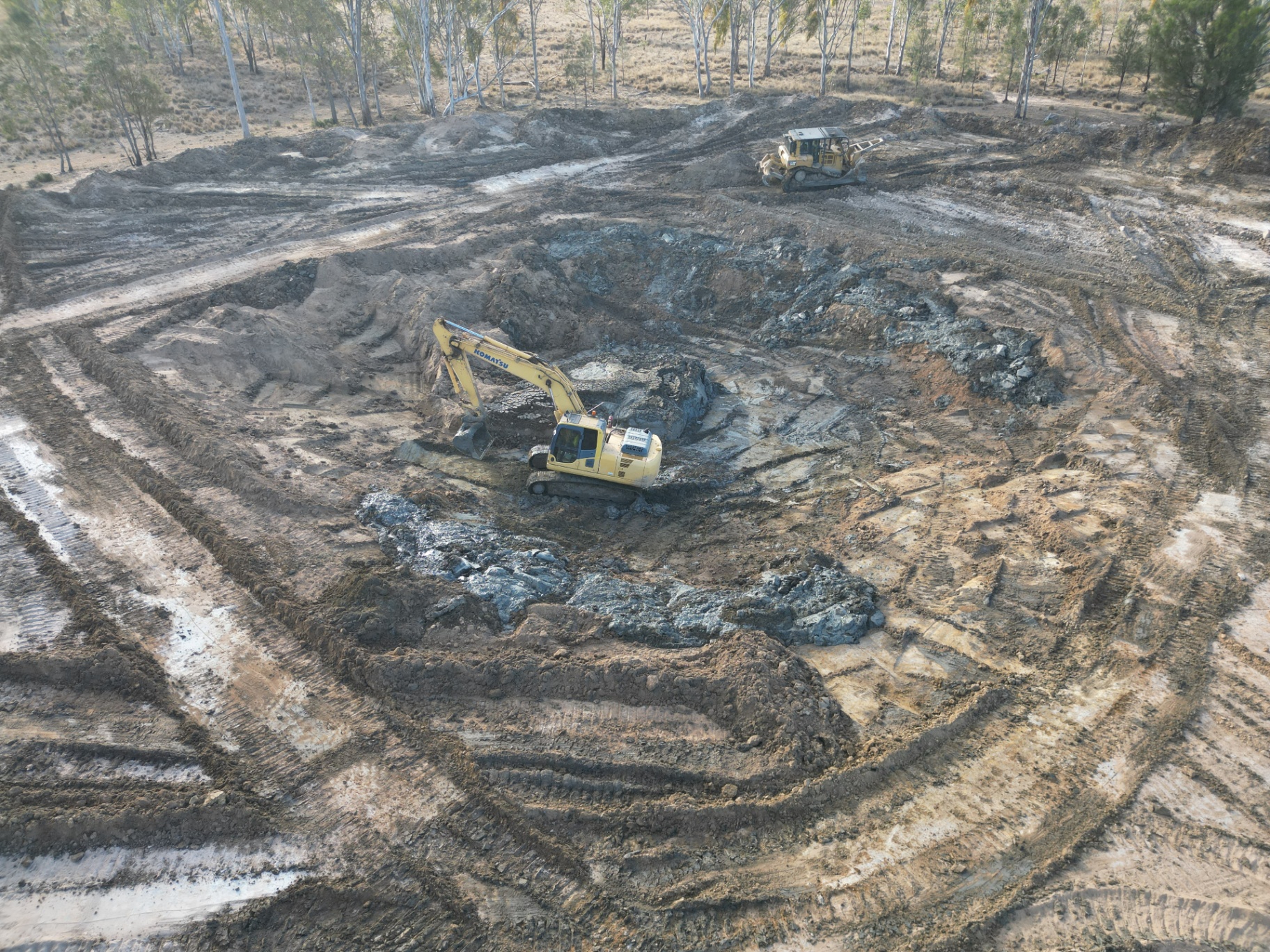 Aerial view of a Komatsu excavator pulling silt from a dam with a CAT dozer pushing spoil on the bank