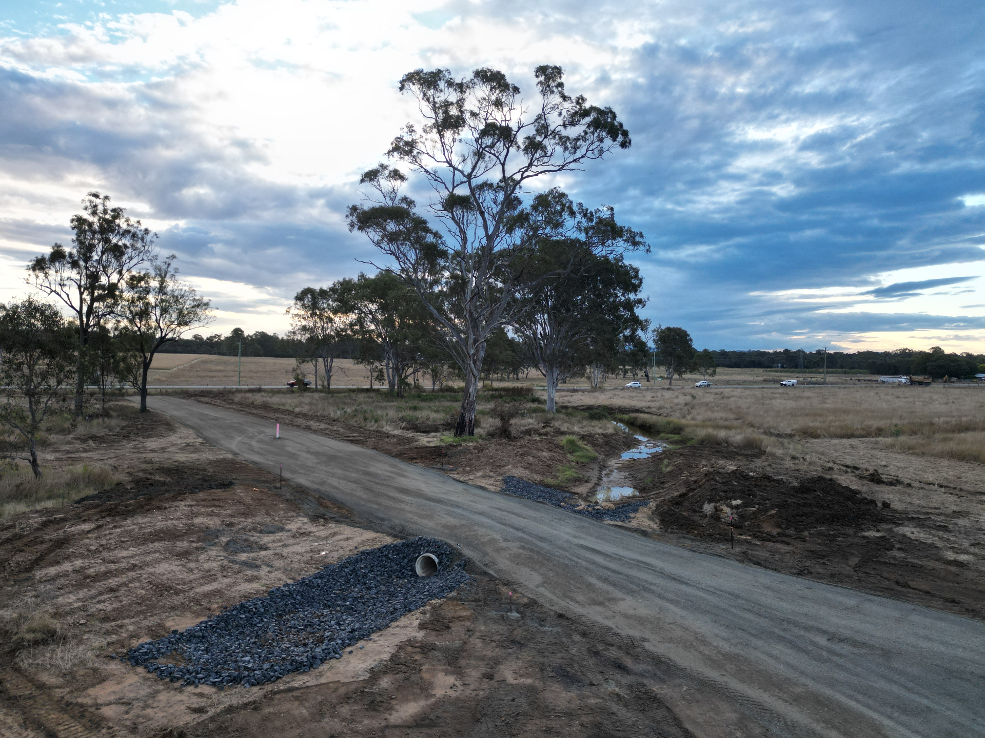 Newly formed gravel access road with culvert and rock pitching beside a gum tree at dusk