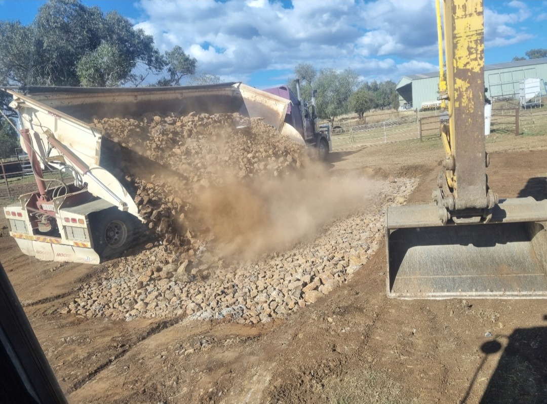 Moore side-tipper unloading rock onto a rural pad with excavator bucket alongside